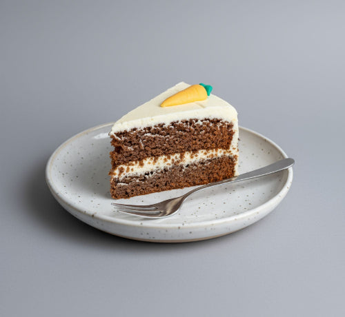 Slice of carrot cake on a plate with a fork against a gray background