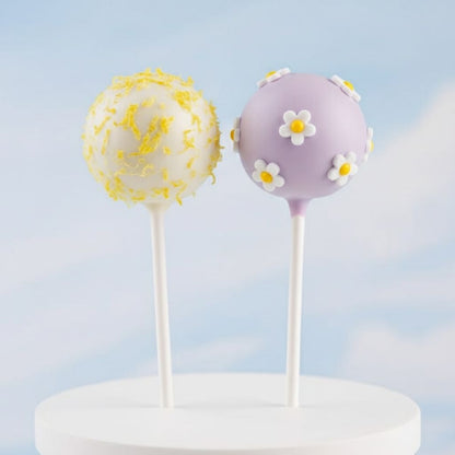 Two cake pops on sticks with decorative elements against a light blue background