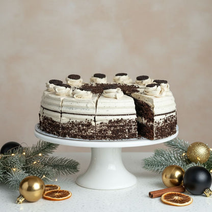 Chocolate cake with white frosting on a white cake stand, surrounded by Christmas decorations.