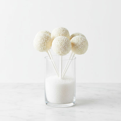 Three white textured ivory cream cake pops in a clear glass on a light gray background