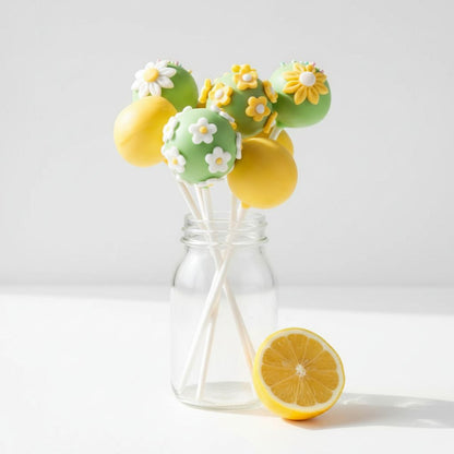 Decorative cake pops with lemon and flower designs in a glass bottle on a white background