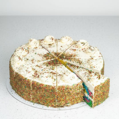 Round rainbow cake with white frosting and a slice removed on a gray background
