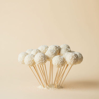 White coconut-covered treats on sticks against a beige background